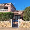 Villa rosa con balcone, cancello blu e cespugli.