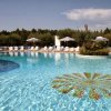 Piscina con sdraio e ombrelloni bianchi, circondata da vegetazione.