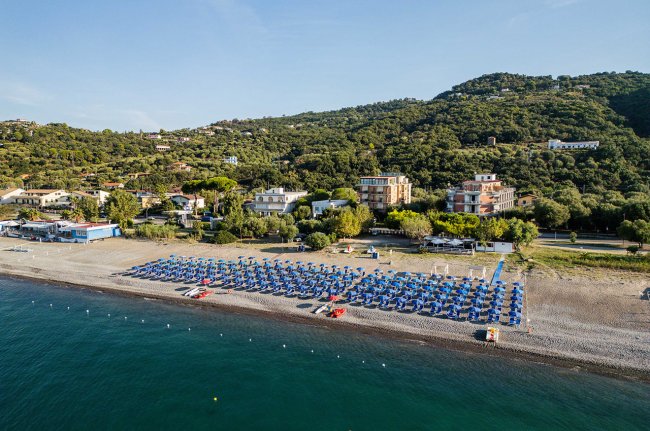 Spiaggia con file di ombrelloni e edifici sullo sfondo.