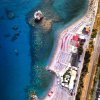 Vista aerea di una spiaggia con ombrelloni e mare azzurro, stradina costiera.