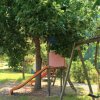 Parco giochi all'aperto con uno scivolo arancione sotto un albero e un'altalena accanto.