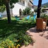 Un giardino con sedie azzurre, una poltrona di vimini, amache e fiori gialli.