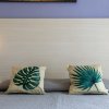 Letto con cuscini a tema foglie tropicali, lampade moderne e un piccolo vaso di piante.