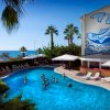 Piscina all'aperto con bagnanti, vista del mare e murale di un pesce blu sull'edificio.