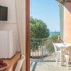 Tavolo e sedie sul balcone con vista mare, TV e frigorifero accanto a una ciotola di frutta.