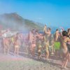 Persone festeggiano sulla spiaggia lanciando polveri colorate.