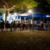 Persone sedute a tavoli all'aperto, illuminate da luci notturne.