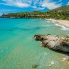 Spiaggia con mare turchese, sabbia chiara e scogli.