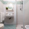 Bagno con doccia, lavabo con specchio rotondo e piastrelle verdi.