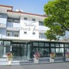 Facciata di un hotel con vetrate, fioriere e un grande albero a destra.