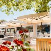 Un patio con sedie, tavoli e ombrelloni bianchi, circondato da rose rosse e alberi.