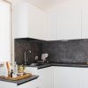 Cucina moderna con mobili bianchi e piano di lavoro scuro, provvista di alcuni utensili e bottiglie.