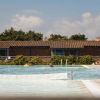Persone rilassate in piscina all'aperto con edifici di legno sullo sfondo.