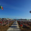 Spiaggia con lettini e ombrelloni colorati, bandiera italiana al vento.
