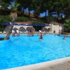 Piscina all'aperto con persone che nuotano, circondata da palme e lettini.