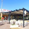 Ristorante con tavoli all'aperto sotto un pergolato, persone che camminano vicino.
