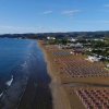 Spiaggia lunga con ombrelloni allineati, mare e colline sullo sfondo.