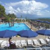 Piscina all'aperto con lettini e ombrelloni blu, vista sul mare e cielo nuvoloso.