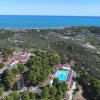 Vista aerea di una collina verde con piscina e vista sul mare azzurro.