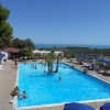 Piscina all'aperto con ombrelloni blu, vista sul mare e paesaggio collinare.