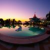 Piscina riflette il tramonto con palme sullo sfondo.