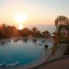 Piscina al tramonto con palme e mare sullo sfondo.