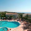 Piscina affollata con ombrelloni, palme e vista sul mare.