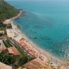 Vista aerea di spiaggia con ombrelloni e mare cristallino.