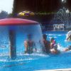 Piscina con giochi d'acqua e persone che nuotano.