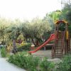 Area giochi con scivolo arancione e alberi intorno.