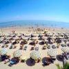 Spiaggia affollata con ombrelloni a righe bianche e gialle.