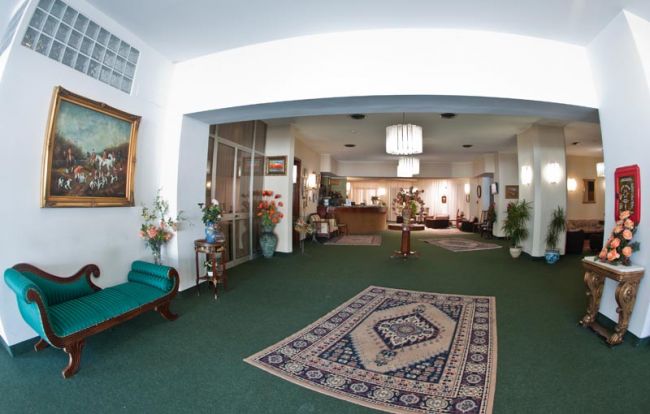 Salone albergo con divano, tappeti e quadri.