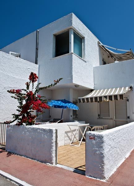 Casa bianca con veranda, ombrellone blu e piante.