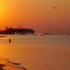 Spiaggia al tramonto con sole arancione e persone in acqua.