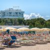 Spiaggia con lettini e ombrelloni, hotel bianco sullo sfondo.