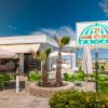 Un bar sulla spiaggia con tavolini verdi e palme.