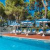 Sedie a sdraio bianche accanto a una piscina, circondate da alberi e ombrelloni.
