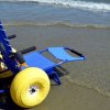 Sedia a rotelle da spiaggia blu con grandi ruote gialle sulla riva.