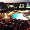 Piscina illuminata di sera, tavoli apparecchiati intorno.