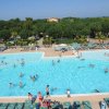 Piscina affollata con scivolo arancione e lettini verdi intorno.