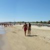 Spiaggia affollata con bagnanti che camminano sulla riva.