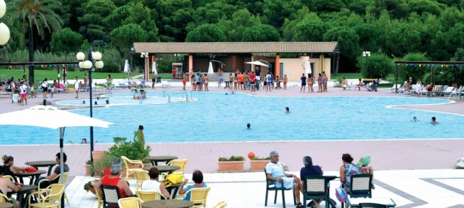 Piscina affollata con sedie e tavolini intorno.