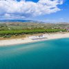 Spiaggia sabbiosa con ombrelloni blu, mare e montagne.