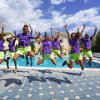 Gruppo salta davanti a una piscina, cielo nuvoloso.
