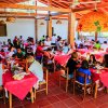 Sala da pranzo affollata con tavoli coperti da tovaglie rosse.