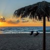 Tramonto su una spiaggia con sedie a sdraio e un ombrellone di paglia.