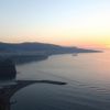 Tramonto su mare calmo e costa collinare.