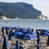 Spiaggia con lettini e ombrelloni blu vicino a un promontorio verde.