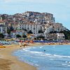 Spiaggia affollata con case bianche in lontananza.