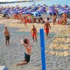 Persone giocano a pallavolo sulla spiaggia con ombrelloni colorati.